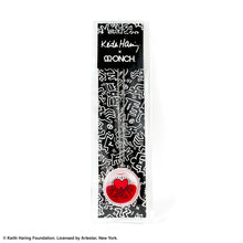 Load image into Gallery viewer, Keith Haring art with three men holding up red heart printed on round clear acrylic pendant filled with red liquid inside a black and white all over print by Kieth haring packaging with collaboration logo with designer ONCH
